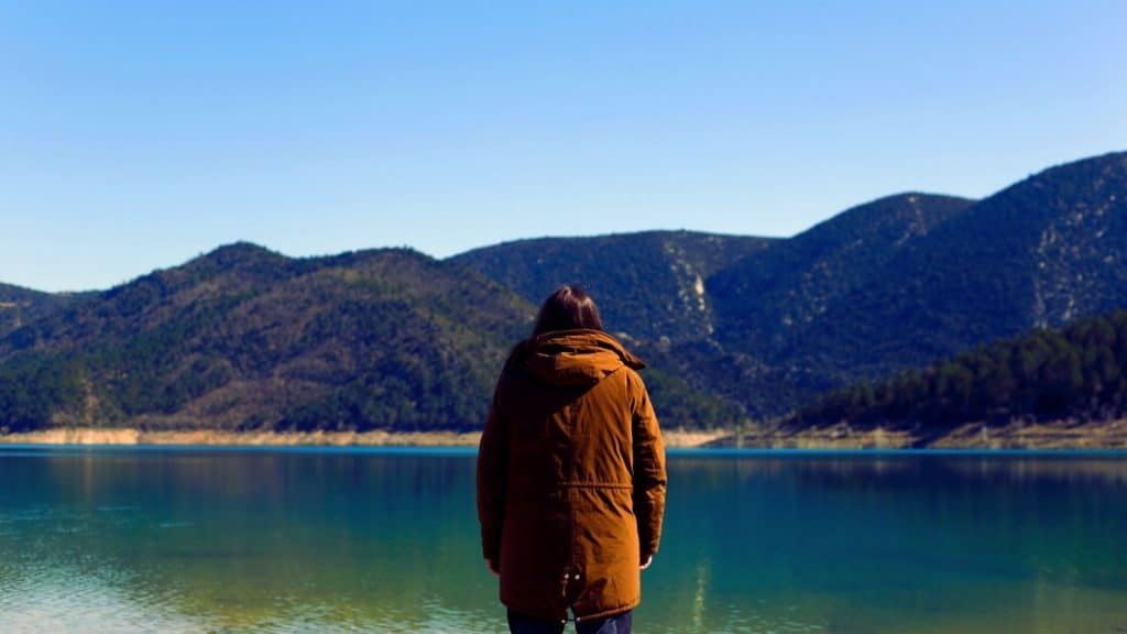 Person standing quietly by a lake, reflecting on their relationship with alcohol