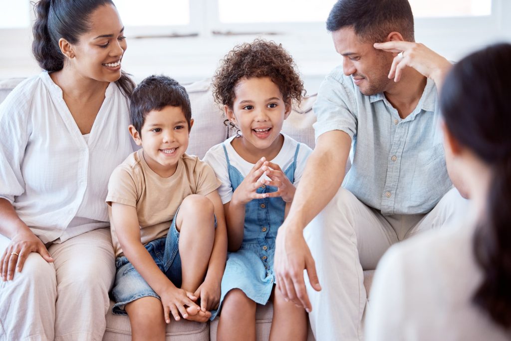Parents and two young children sitting on a couch talking with a therapist