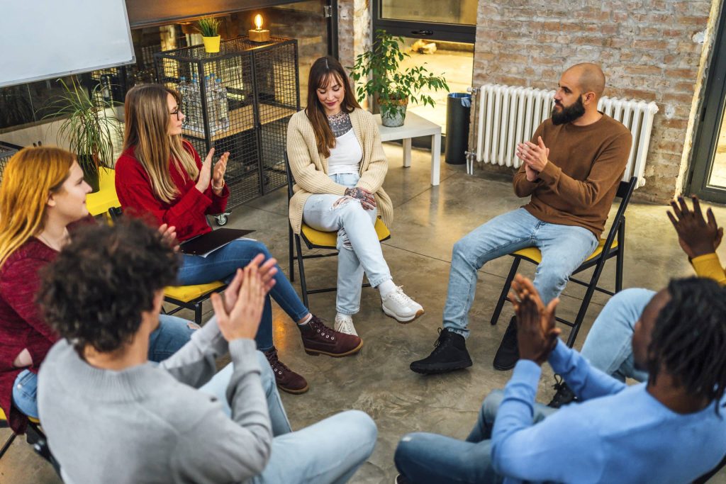 Members of a support group applauding in a circle of chairs