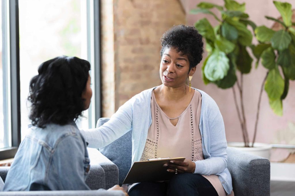 A therapist with a clipboard reaching out to comfort a client during a session