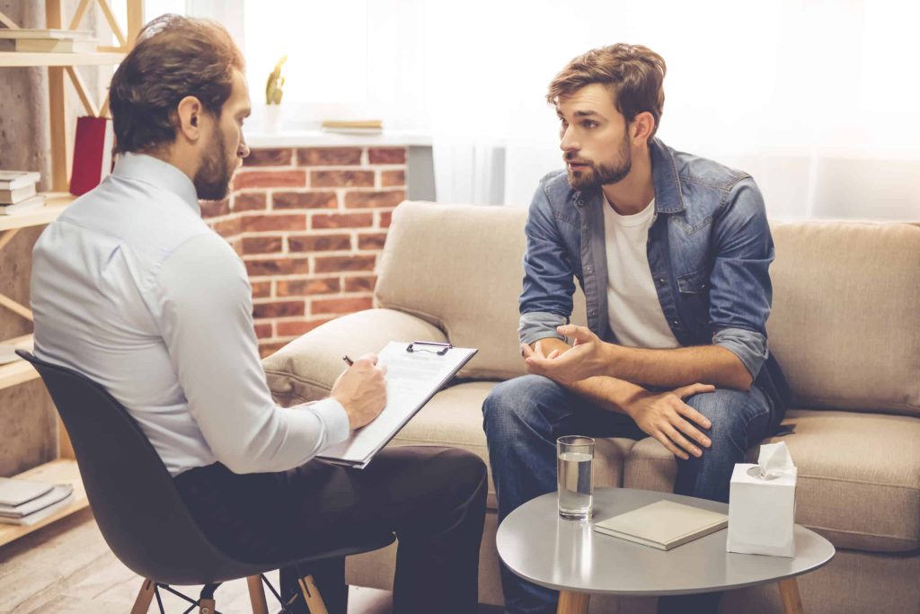 A therapist taking notes during a one-on-one session with a young man on a couch