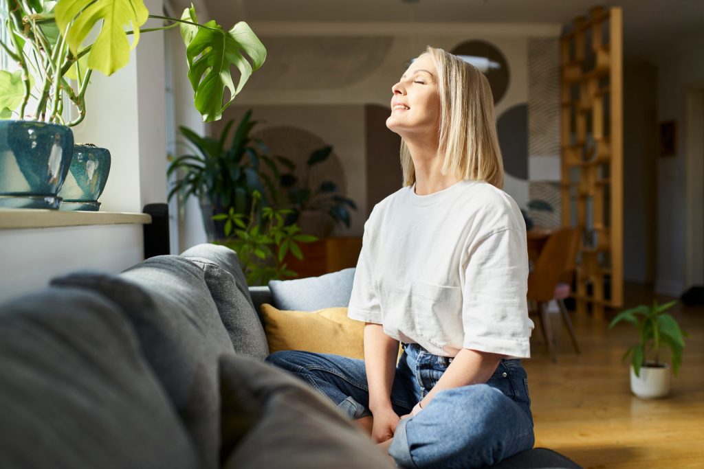 A woman sitting on her living room couch with her eyes closed in the sunlight
